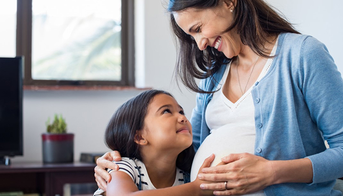 Pregnant women sitting with young daughter on couch