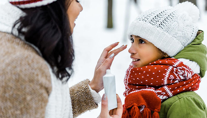 Woman applying sunscreen to a child in a winter setting