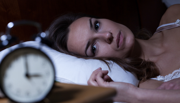 Woman looking anxiously at alarm clock