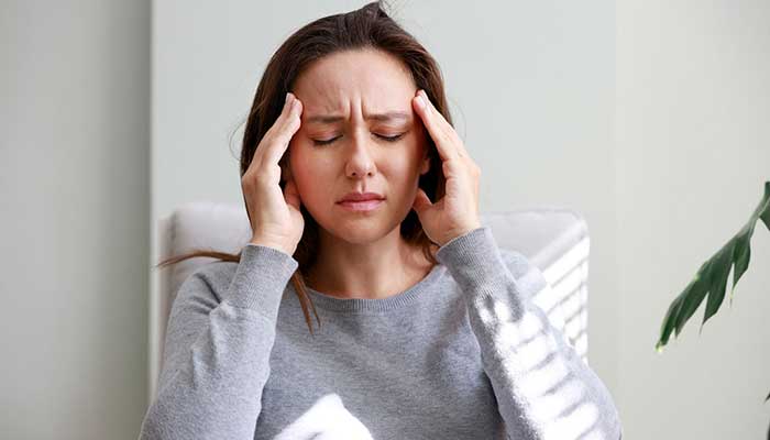 A young woman in pain holds her head