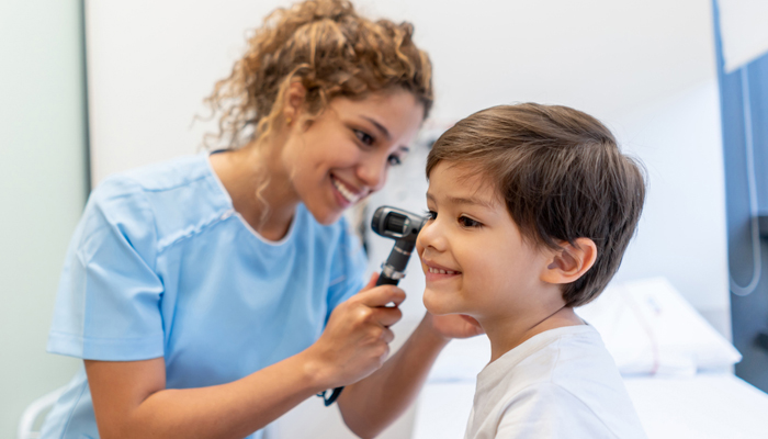 Female healthcare provider checking ear of young boy in exam room