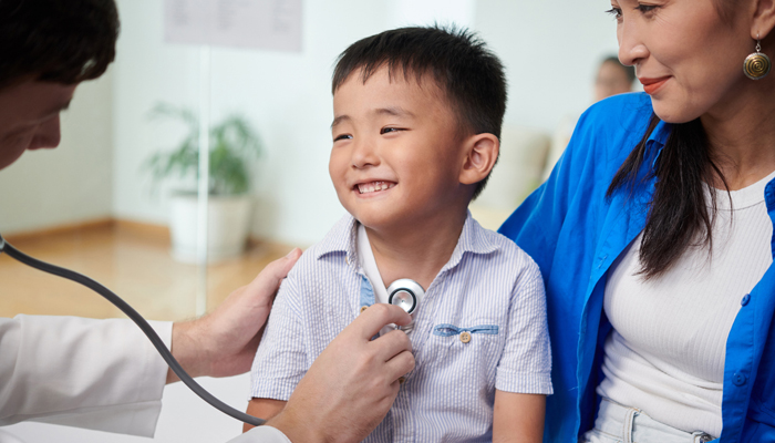 Male healthcare provider using stehescope on young boy while mother observes