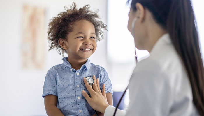 Female healthcare provider using stethescope on young boy